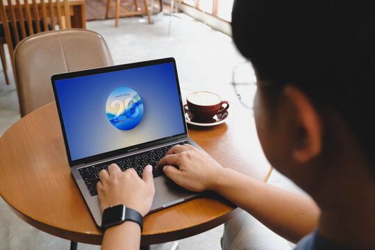 Bangkok, Thailand. July 12, 2026; A close-up view of a person typing on a MacBook Pro laptop displaying the macOS Tahoe operating system interface on the screen at a wooden cafe table.