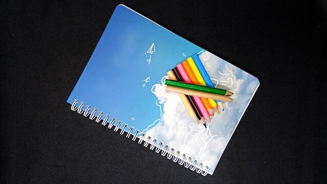 Open blank notebook and sharp colored pencils arranged neatly showcasing vibrant rainbow hues and clean white pages flat lay top view studio shot with bright soft daylight minimal lighting for art edu