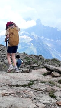 Young boy hiking on a rocky mountain path with a backpack, admiring the stunning alpine panorama with the aiguille du g&eacute;ant peak against a cloudy sky during summer