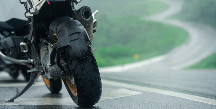 Motorcycle with worn tires stands on wet road, suggesting rainy day ride through winding paths