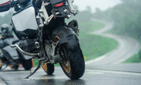 Adventure motorcycle parked on wet road during rainy day, with winding road in background