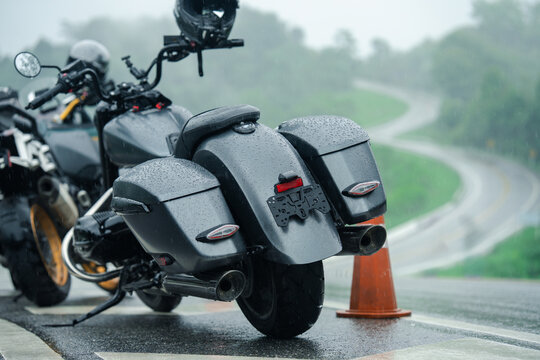 Motorcycles parked on rainy day with wet surfaces and winding road in background