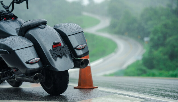 Motorcycle parked on wet road with traffic cone nearby, surrounded by lush greenery and winding road in background