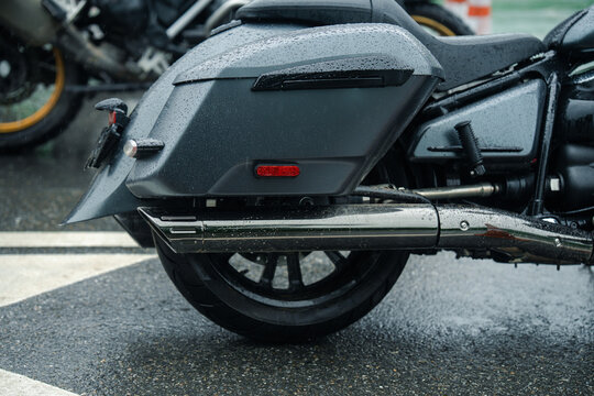 Sleek motorcycle parked on wet road, showcasing its rear wheel and exhaust pipe, with raindrops adding dramatic touch
