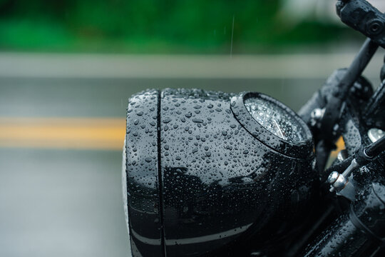 Close up of motorcycle headlight covered in raindrops, reflecting moody atmosphere