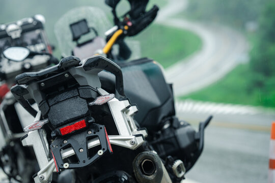 Motorcycles parked on rainy day with winding road in background, evoking sense of adventure