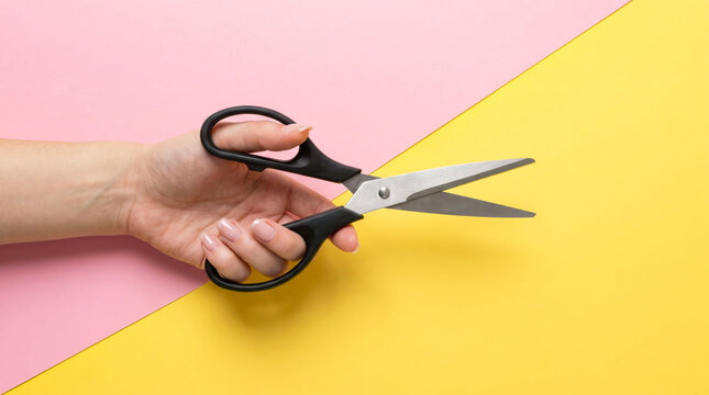 Hand cutting paper with black scissors on colorful background