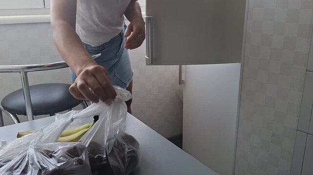 A person opens the refrigerator in the kitchen and moves bags of groceries into it.