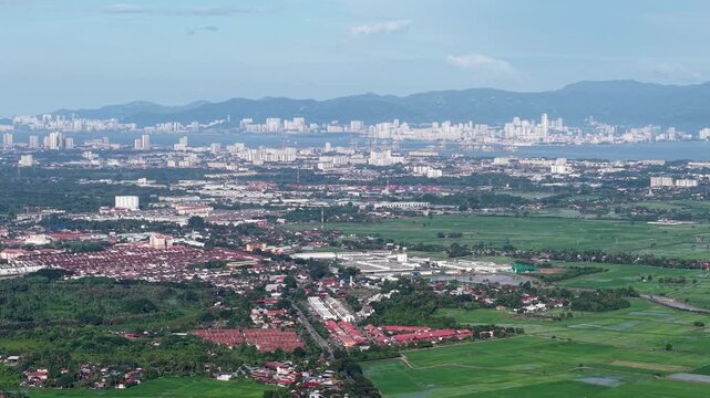 An expansive aerial shot showing a blend of urban cityscape, green countryside, and distant mountains under a partly cloudy sky at Kubang Semang