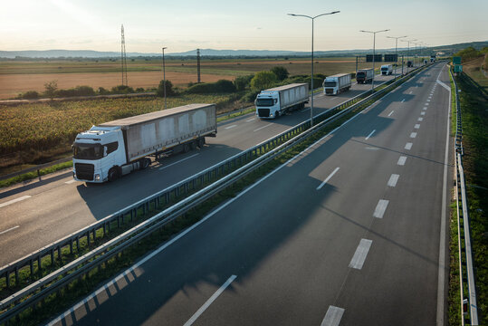 Convoy of transportation trucks with grey containers on highway, cargo transportation concept in springtime - freight service, with a dramatic sunset sky in background