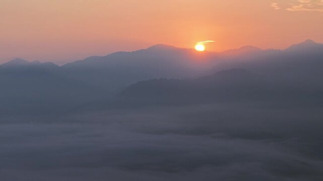 Sunrise glows over distant mountains. Warm orange light illuminates the scene at Lenggong, Malaysia