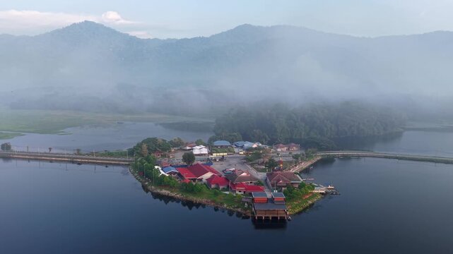Aerial shot of a small island with traditional buildings surrounded by calm lake water at Tasik Raban