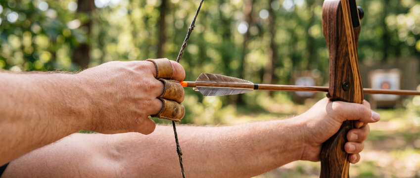 Experienced archer drawing wooden bow and arrow in outdoor target practice in woodland range