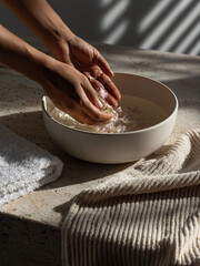 Fototapeta premium Close up of hands placing flowers in a white ceramic bowl of warm water