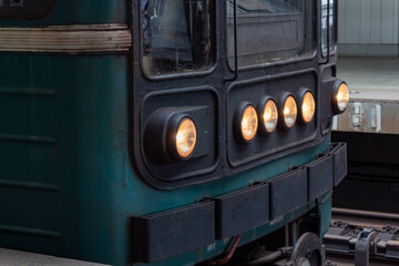 Front view of old green train locomotive with glowing yellow headlights in depot © PhotoBank