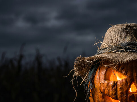Halloween pumpkin with straw hat against dark cloudy background  