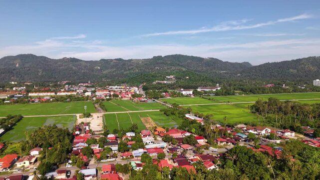 Aerial perspective of a rural village surrounded by green farmland, trees, and a distant mountain range under a clear blue sky at Balik Pulau