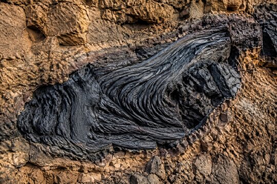 Cross-section of cooled volcanic lava flow fused with bedrock, contrasting textures.