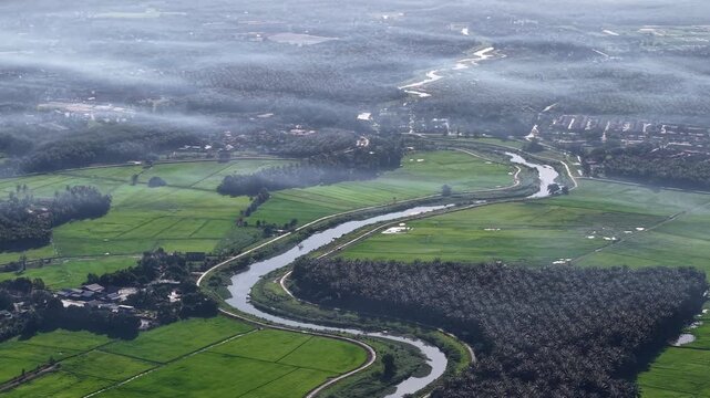 An expansive bird's eye view capturing a winding river flowing through vibrant green farmland at Kubang Semang