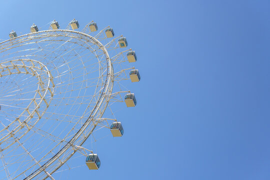 Ferris wheel structure with multiple modern passenger cabins filling the left half of the frame. Clear vivid blue sky providing copy space on the right side.