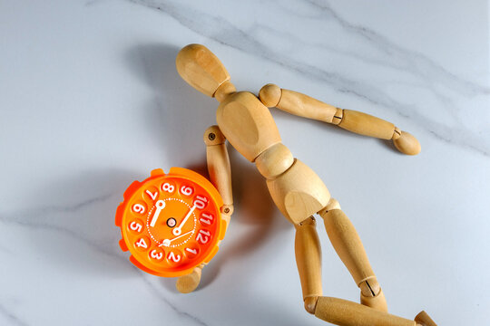 Wooden mannequin lying next to orange alarm clock