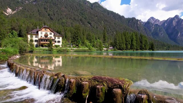 Lago di Dobbiaco Italy 4K Drone. Low altitude sideways tracking flight over calm lake water with waterfall and mountain reflection. Scenic Dolomites landscape b roll cinematic travel stock video