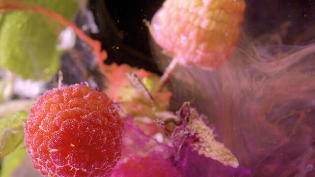 Extreme close-up of ripe raspberries showing detailed bumpy drupelets and frostlike condensation while pink-magenta vapor drifts through dark background
