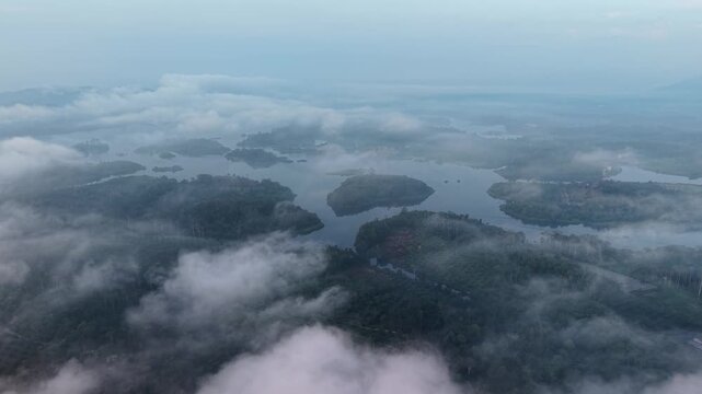 Aerial shot captures mist covered islands surrounded by calm water and dense fog at Tasik Raban