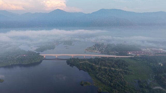 Aerial view captures a long bridge spanning a calm lake in misty day at Tasik Raban