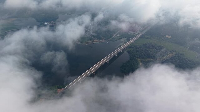 A stunning aerial view of a long bridge extending over a calm river, surrounded by dense clouds and lush green forests, creating a serene and atmospheric landscape. at Tasik Raban
