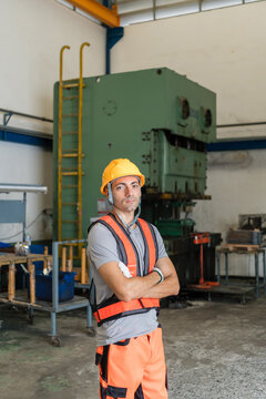confident factory worker standing arms crossed before green power press machine