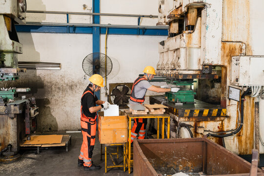 Two workers handling metal panels at rusted industrial power press