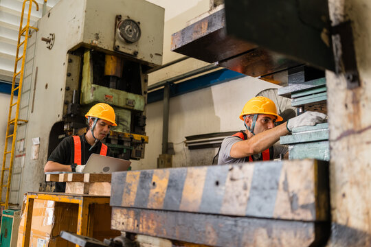 Engineer reviewing laptop data beside colleague adjusting punch press stamping die