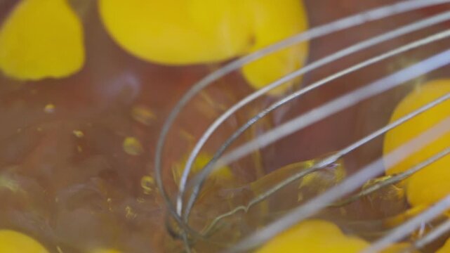 Close up of whisk beating raw eggs in glass bowl for homemade cooking baking meal preparation and culinary recipe ingredients. 
