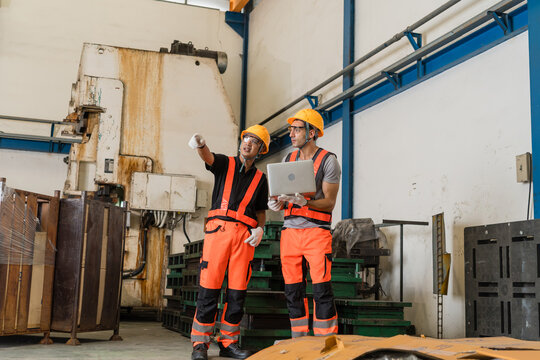 Factory engineers checking laptop inspection data near old power press machine on production floor