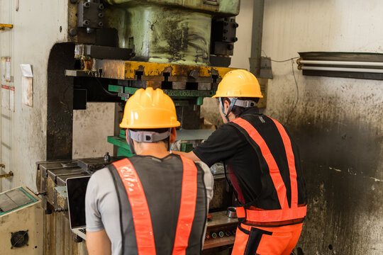 Two factory workers examining stamping press die from behind in machine shop
