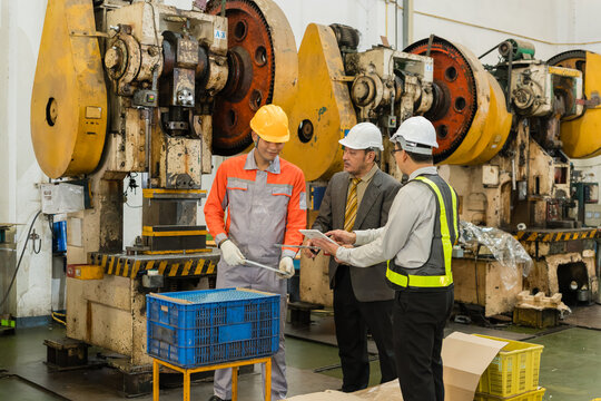 Factory team discussing maintenance schedule on tablet beside stamping press machinery