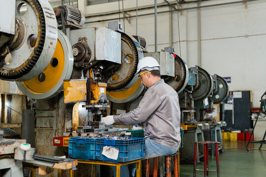Machine operator wearing safety glasses inspecting stamped metal parts at punch press workstation
