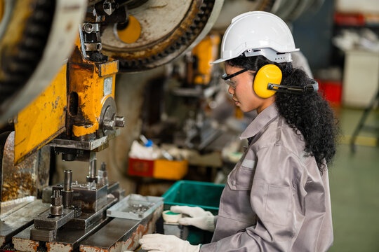 Young female machine operator sorting stamped metal parts beside power press