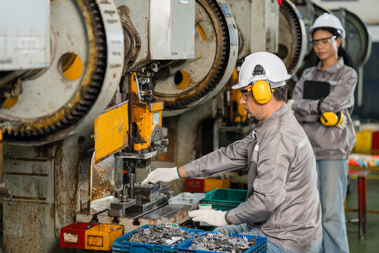 Operator adjusting punch press die while colleague reviews tablet in background