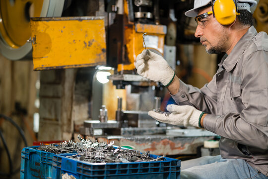 Technician Closely Examining Small Stamped Metal Hook Near Punch Press