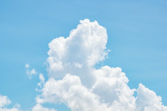 Fluffy white cumulus clouds floating in clear blue sky. Bright atmospheric sky background with soft natural lighting.