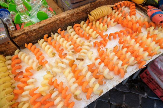 Rows of fresh spiralized potatoes and carrots displayed at a street food market stall ready for frying