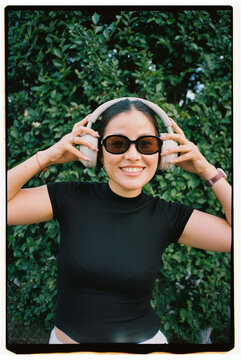 Smiling Woman Putting On Wireless Headphones Outdoors