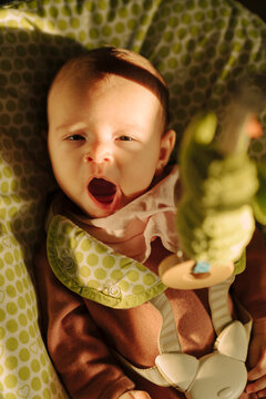 Sleepy yawning baby sitting in a bouncer seat