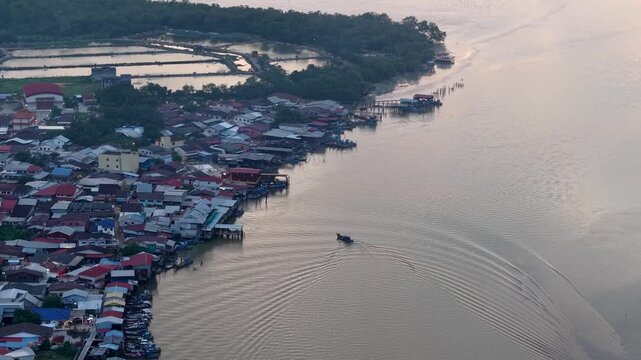 Aerial view of a riverside village at dawn. Single boat glides across the calm water at Sungai Udang, Penang