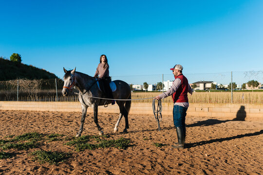 Girl learning to ride horse with trainer