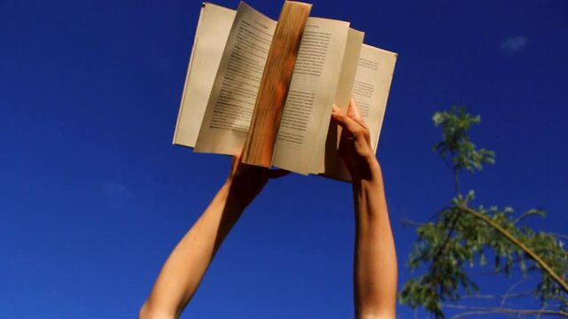 Book in woman hands against blue sky at low angle. Bright image for book shops, articles
