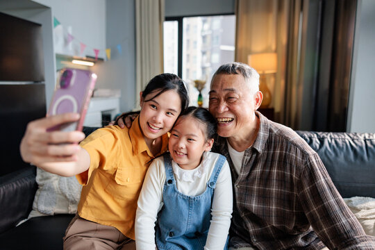 Three generations smiling for a selfie together at home.