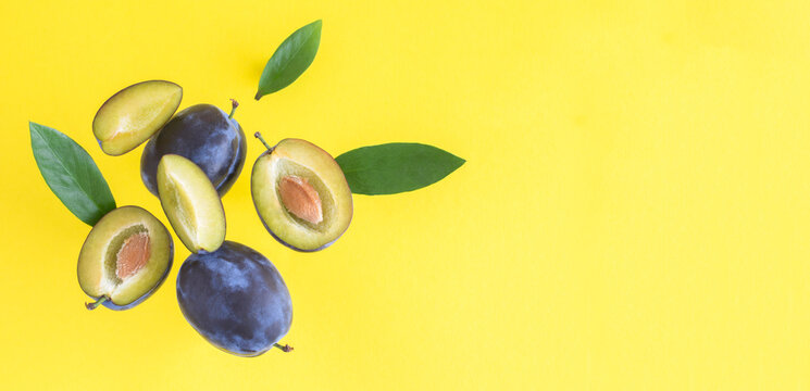 Flying in air fresh ripe whole and cut blue plums with leavs on a yellow background. Top view. Copy space.